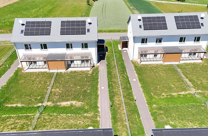 Zwei moderne Häuser mit Solaranlagen auf den Dächern und kleinen Gärten.
