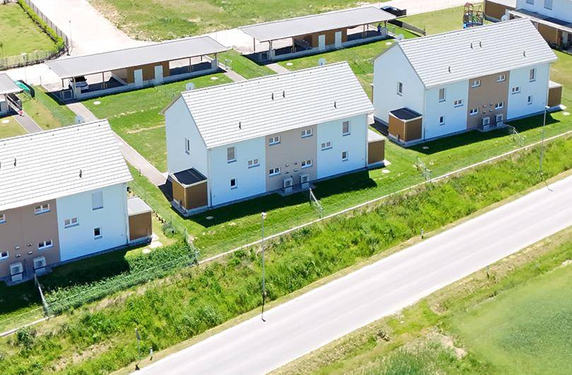 Luftaufnahme einer Siedlung mit modernen Einfamilienhäusern, grünen Gärten und Carports.
