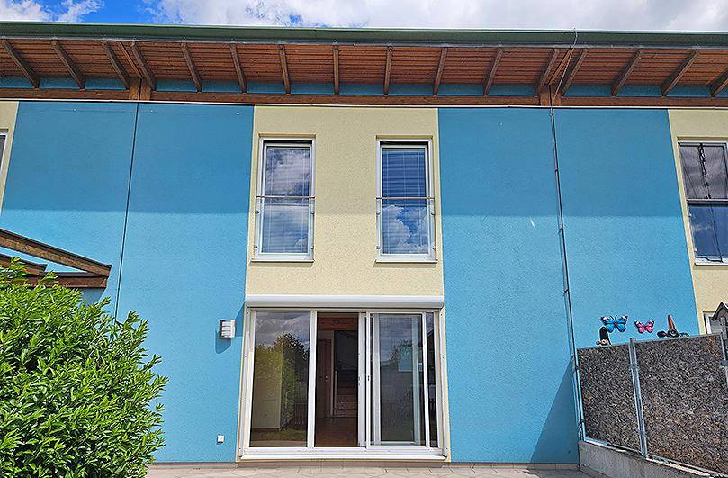 Moderne Gebäudefassade mit blauen und beigen Akzenten, einer Terrasse und französischen Balkonen.