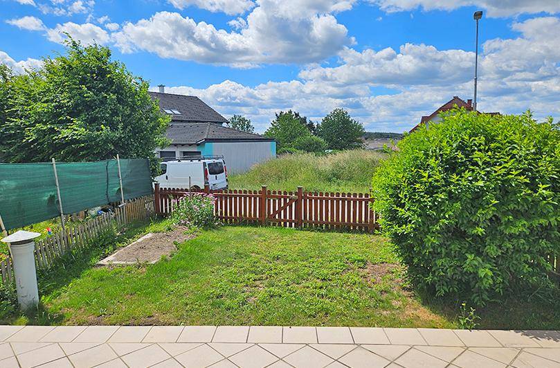 Kleiner, eingezäunter Gartenbereich mit Rasenfläche und Büschen unter blauem Himmel.
