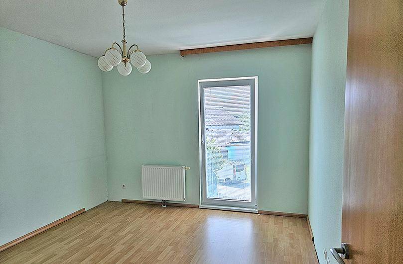 Geräumiges Zimmer mit hellgrünen Wänden, Laminatboden und Zugang nach draußen.