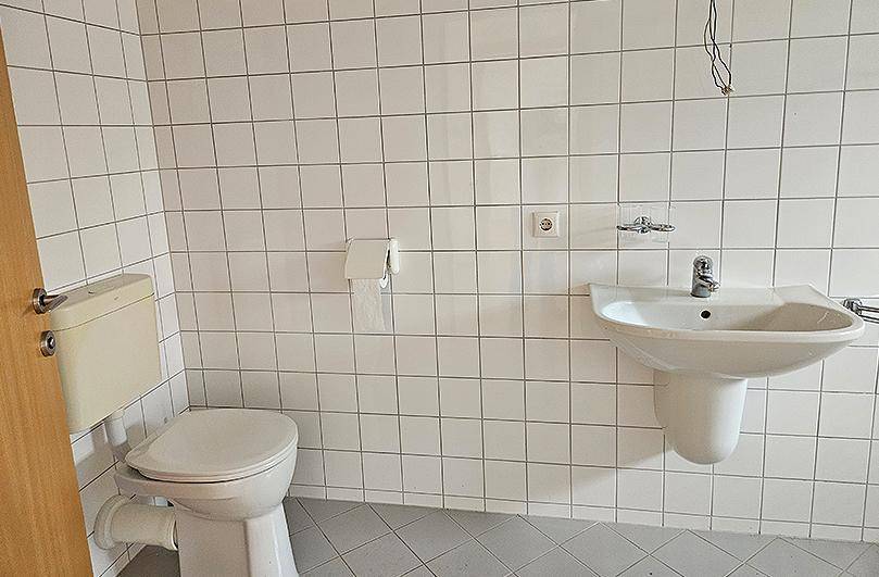 Einfaches WC mit weißen Fliesen, Toilette und Waschbecken.