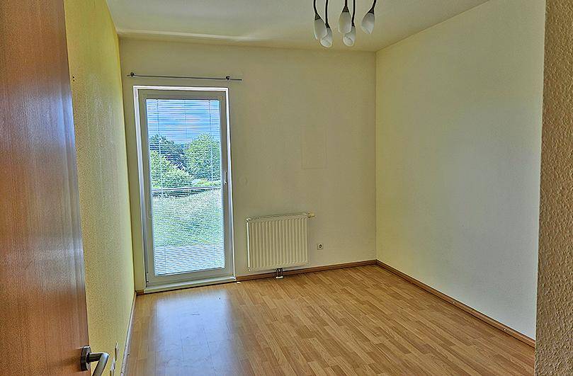 Helles Zimmer mit Laminatboden und Zugang zu einem kleinen Balkon oder Gartenbereich.