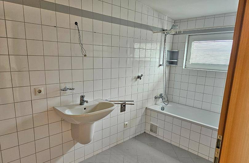 Badezimmer mit Badewanne, Waschbecken, Fenster und weißen Wandfliesen.