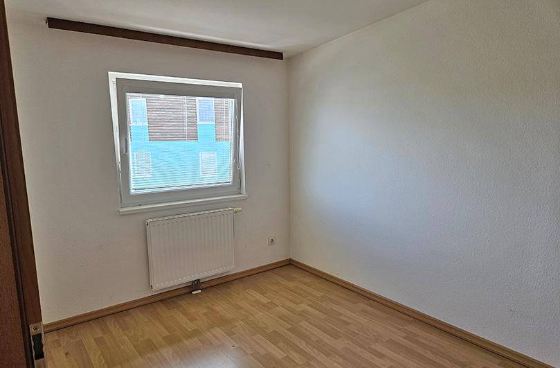 Leeres Zimmer mit Laminatboden, einem Fenster und einem Heizkörper.