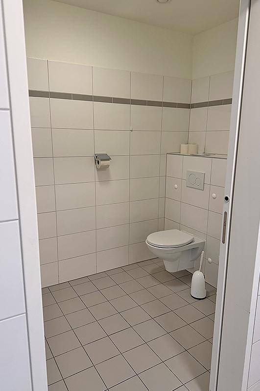 Sauberer und funktionaler WC-Raum mit wandhängender Toilette und hellen Fliesen.