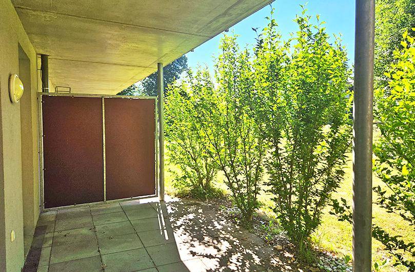 Überdachte Terrasse mit Sichtschutz und grüner Bepflanzung im Außenbereich.