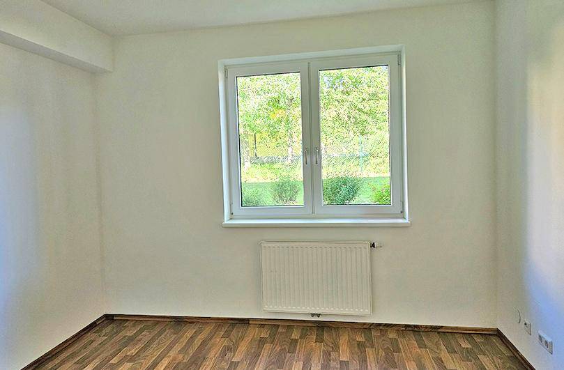 Schlafzimmer mit Laminatboden, großem Fenster und Blick ins Grüne.