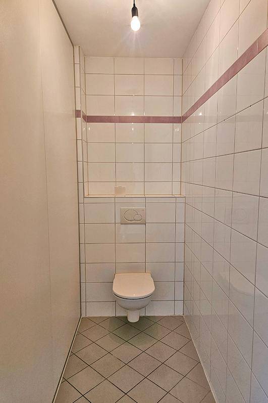Separate Toilette mit weißen Fliesen, Wand-WC und dekorativer rosa Bordüre.