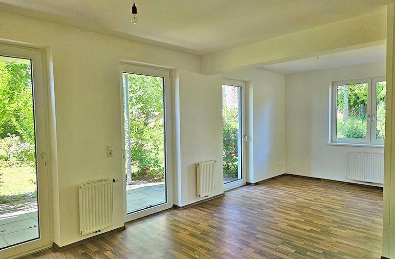 Helles Zimmer mit Laminatboden und mehreren Zugängen zur Terrasse oder zum Garten.