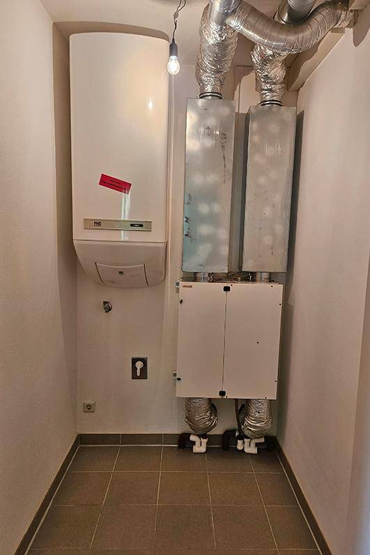 Technikraum mit Heizungsanlage und Lüftungssystemen auf Fliesenboden.