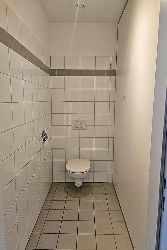 Modern gefliestes Gäste-WC mit wandhängender Toilette und schlichtem Design.