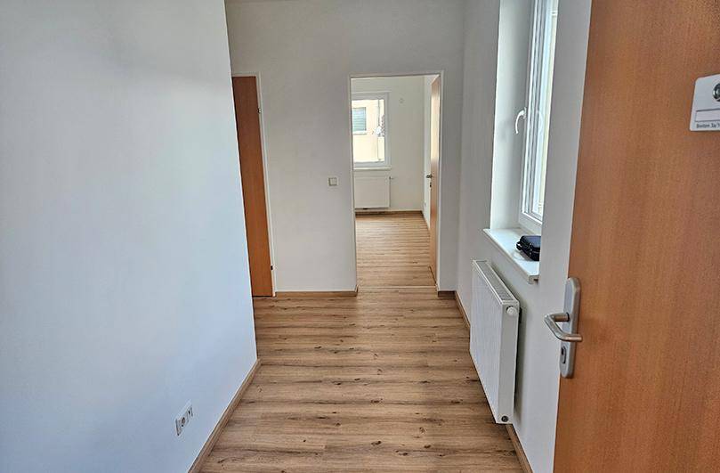 Heller Flur mit Laminatboden, der zu weiteren Zimmern und einem Fenster führt.