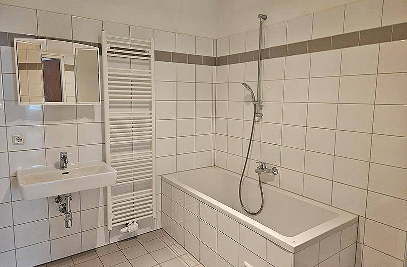 Gefliestes Badezimmer mit Badewanne, Waschbecken und beheiztem Handtuchhalter.