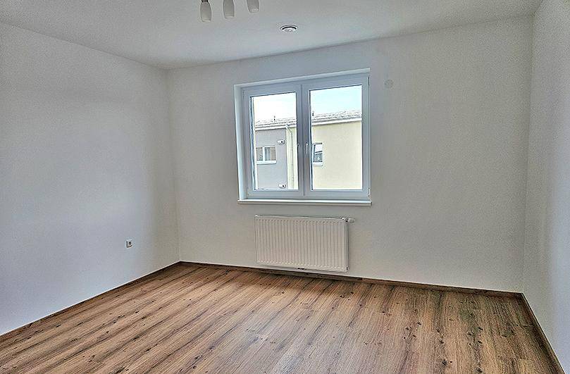 Einfaches, helles Zimmer mit Laminatboden und einem Fenster mit Blick auf Nachbargebäude.