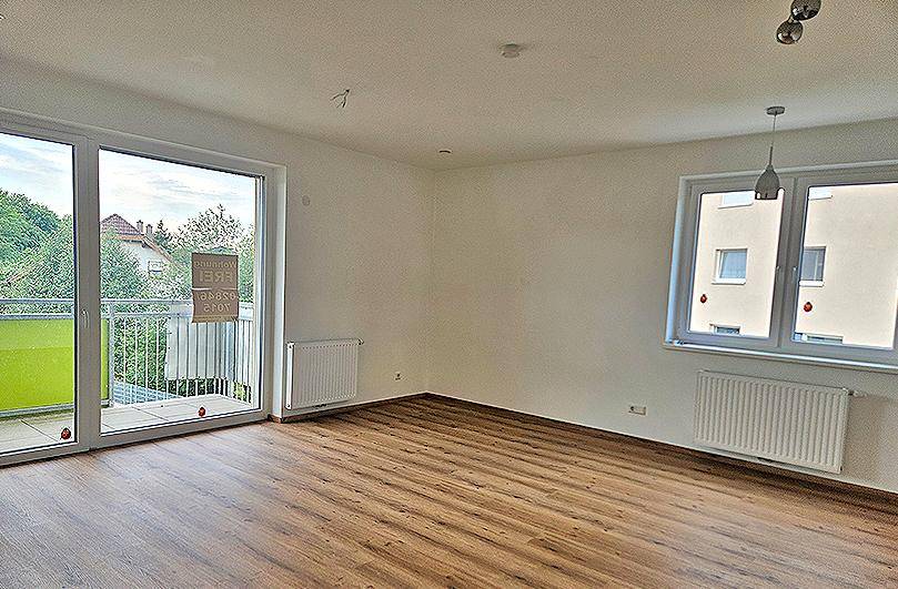 Heller Wohnraum mit Laminatboden und großem Fenster mit Zugang zu einem Balkon.