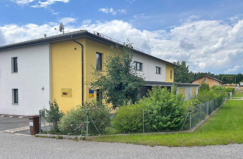 Seitenansicht eines modernen Wohngebäudes mit gelber und weißer Fassade und gepflegter Grünfläche.