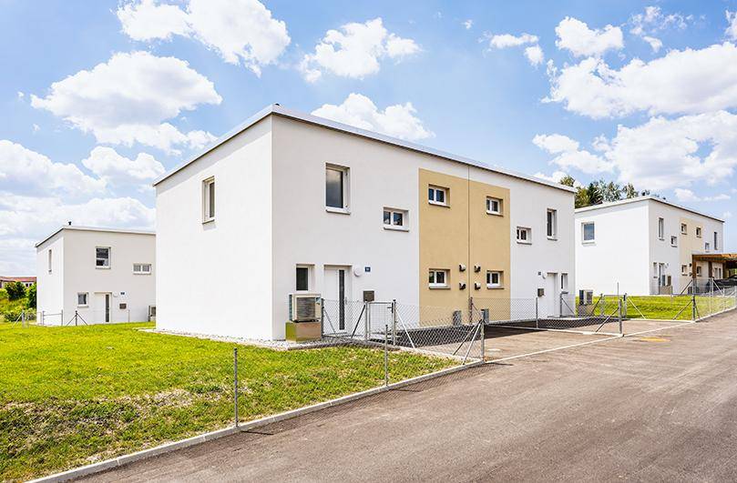 Moderne Reihenhäuser mit weißer und beiger Fassade sowie gepflegten Grünflächen.