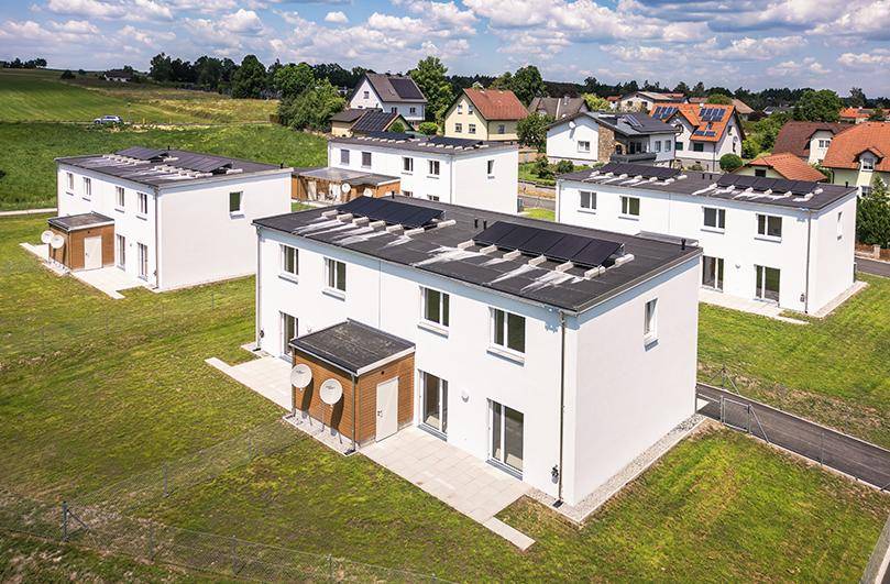 Luftaufnahme von modernen Reihenhäusern mit Photovoltaikanlagen auf den Flachdächern in grüner Landschaft.