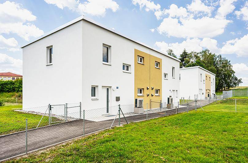 Modernes Reihenhaus mit weißer und gelber Fassade, umgeben von Grünflächen und einem Zaun.