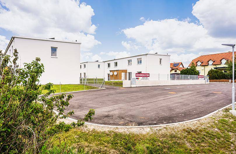 Großer gepflasterter Parkplatz vor modernen Reihenhäusern mit freiem Reihenhaus-Schild.