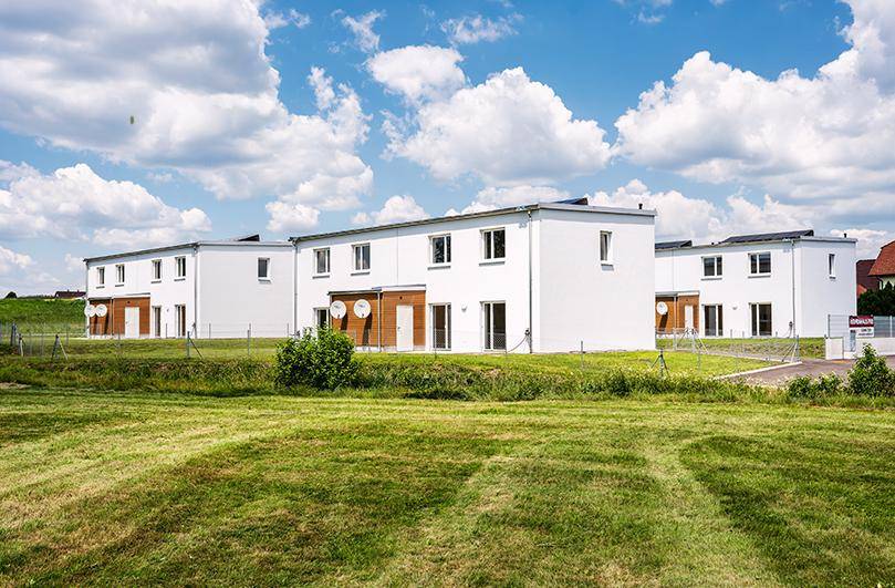 Reihenhäuser mit weißer Fassade und Flachdach in ländlicher Umgebung unter blauem Himmel.