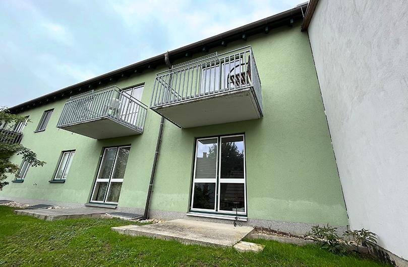 Seitenansicht des grünen Gebäudes mit Balkonen und bodentiefen Fenstern im Erdgeschoss.