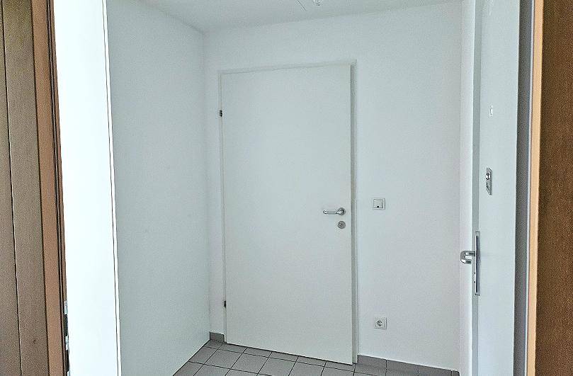 Heller Eingangsbereich mit weißer Tür und praktischem Fliesenboden, der zum Wohnbereich führt.