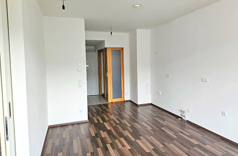 Geräumiger, heller Raum mit dunklem Laminatboden und weiß gestrichenen Wänden, bereit zur Einrichtung.