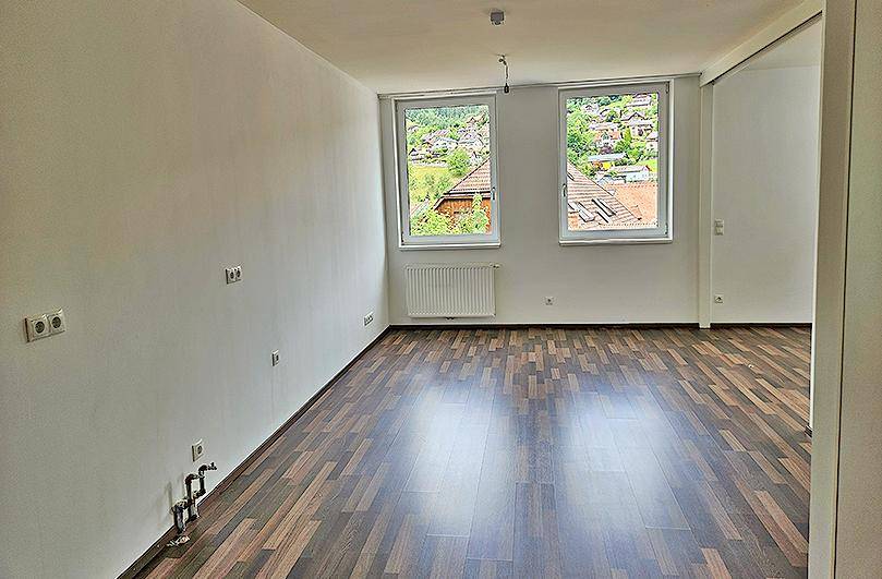 Helles Schlafzimmer mit Laminatboden und Ausblick auf grüne Hügel und die umliegenden Dächer.