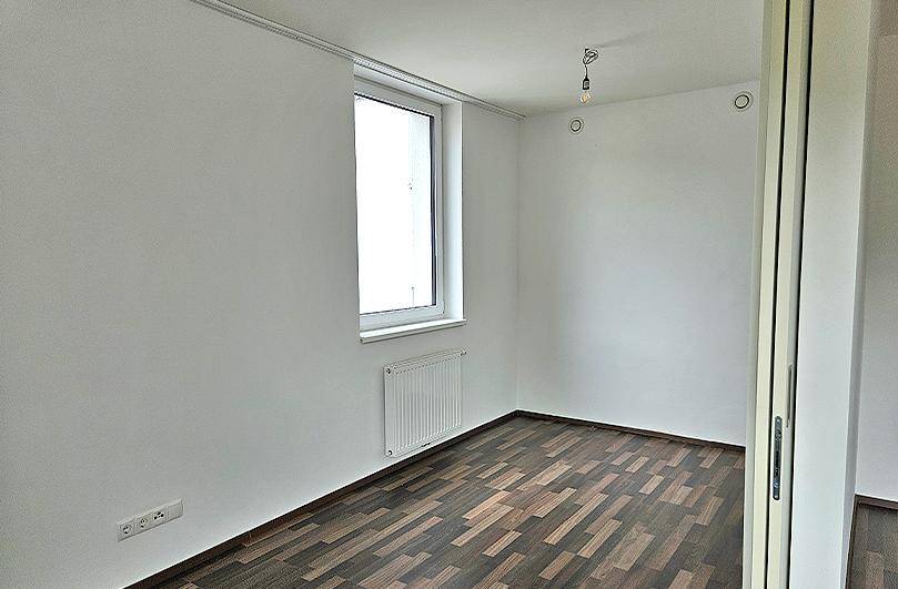 Helles Zimmer mit Laminatboden und einem Fenster, ideal als Schlaf- oder Arbeitszimmer nutzbar.