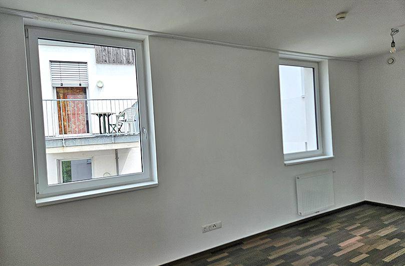 Geräumiger Raum mit Laminatboden und Fenstern, die einen Blick auf einen Balkon bieten.