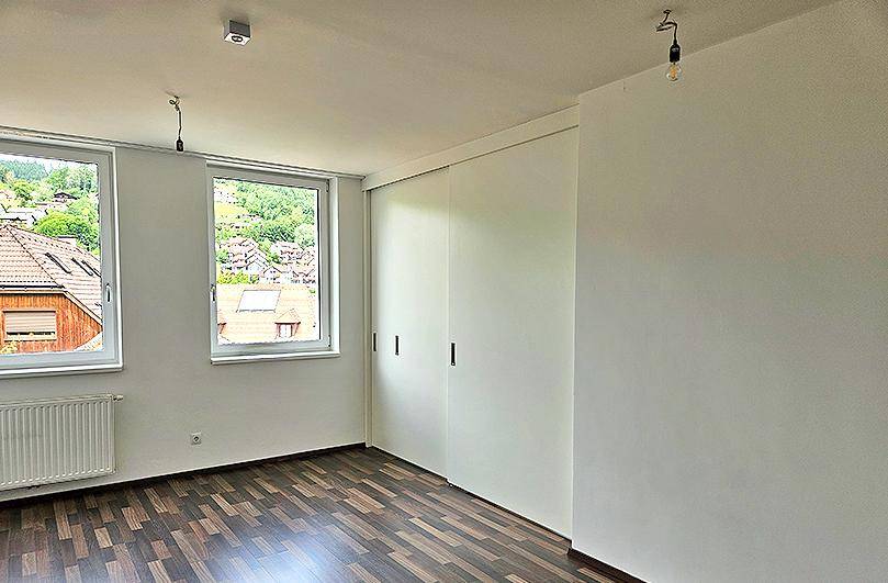 Schlafzimmer mit Laminatboden, Einbauschränken und Blick auf die umliegende grüne Landschaft.