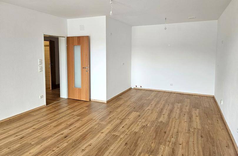 Geräumiges, leeres Wohnzimmer mit Laminatboden und weiß gestrichenen Wänden, bereit zur Gestaltung.