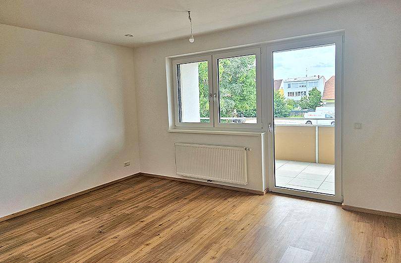 Helles Zimmer mit Laminatboden, Heizkörper und direktem Zugang zu einem Balkon.