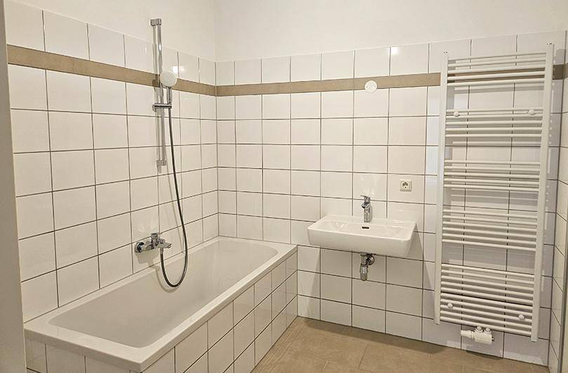Badezimmer mit Badewanne, Waschbecken und einem praktischen beheizten Handtuchhalter.