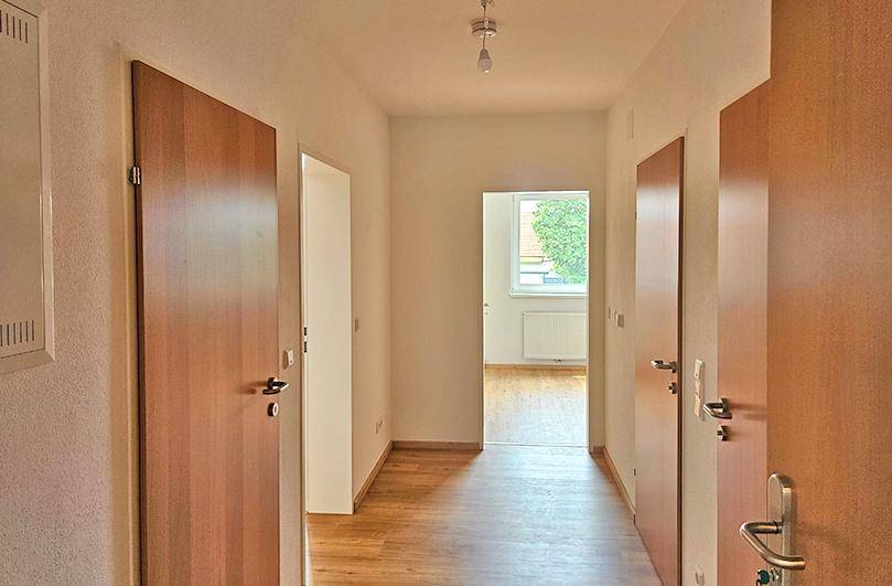 Heller Flur mit Holztüren und Laminatboden, der zu einem weiteren Raum führt.