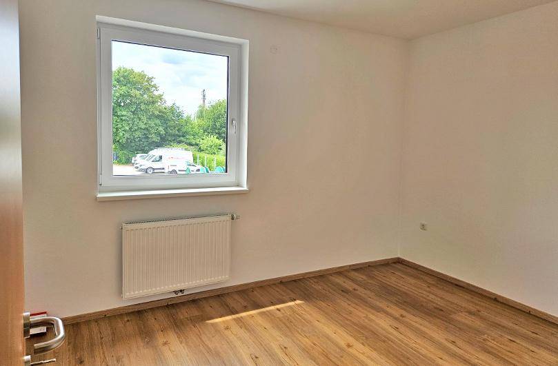 Leeres Zimmer mit Laminatboden und einem Fenster, das viel Tageslicht hereinlässt.