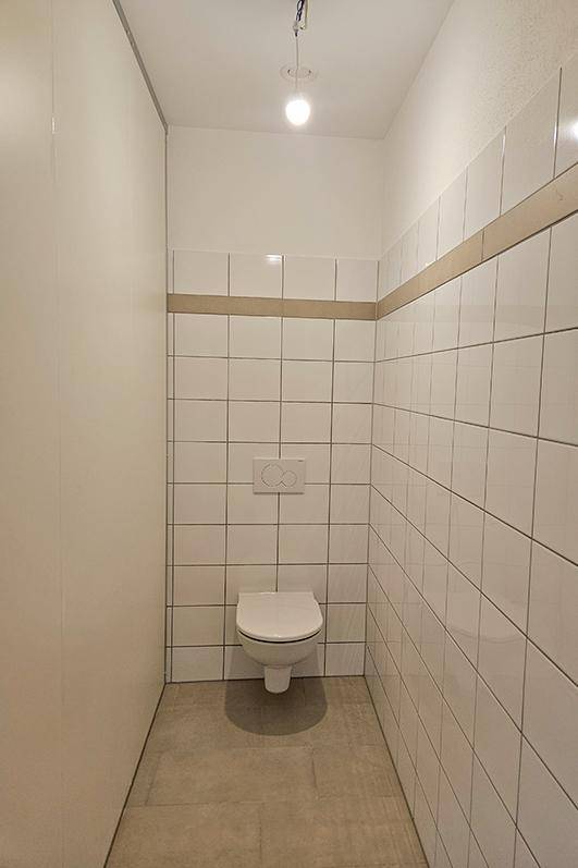 Separates WC mit wandhängender Toilette und weißen Fliesen, sauber und funktional.