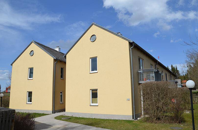 Seitenansicht eines gelben Mehrfamilienhauses mit Satteldach und einem kleinen Balkon.