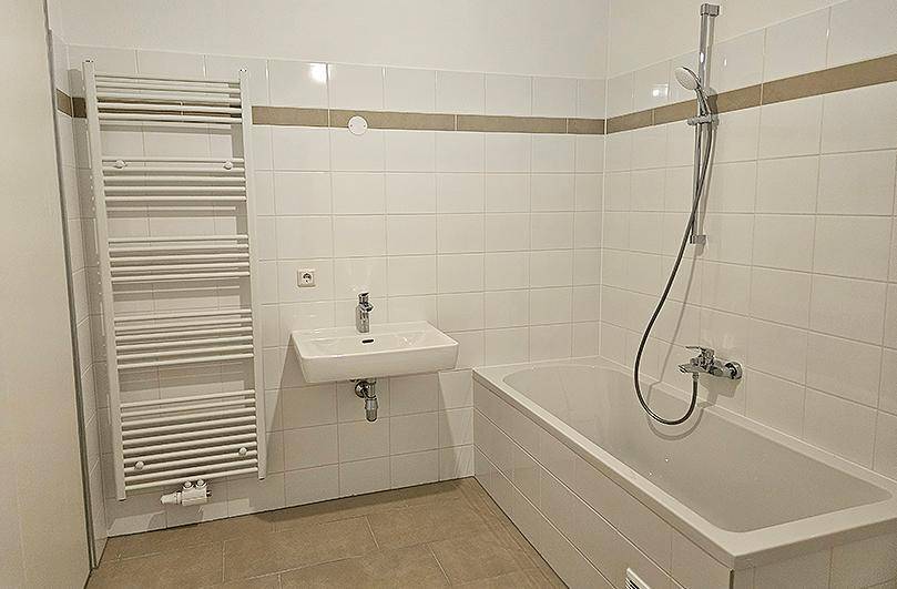 Modernes Badezimmer mit weißen Fliesen, Badewanne mit Duschfunktion und beheiztem Handtuchhalter.