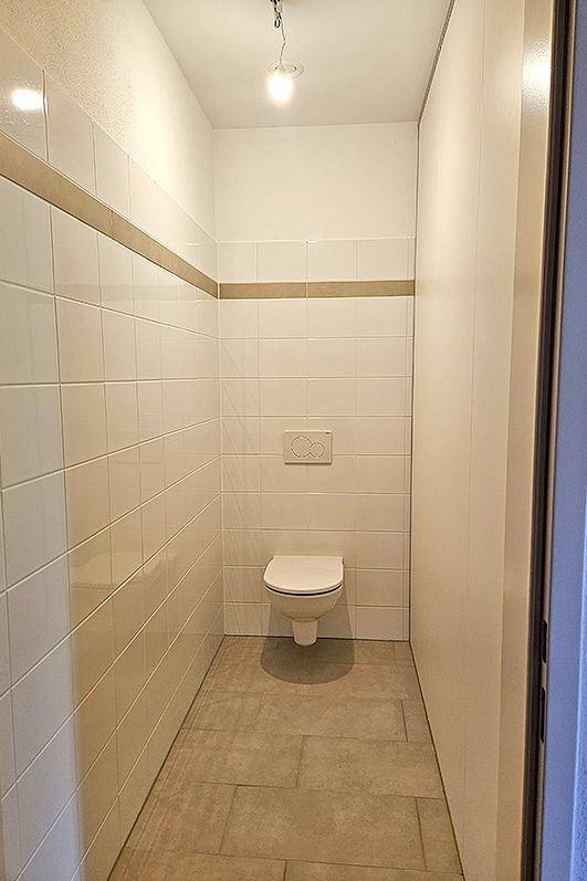 Separates WC mit wandhängender Toilette und weißen Fliesen, praktisch für Gäste.