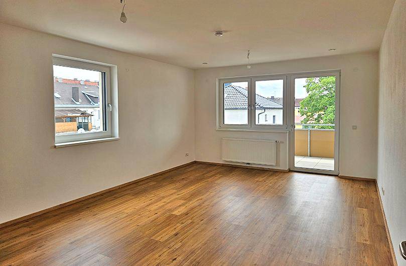 Helles Wohnzimmer mit Laminatboden, großen Fenstern und direktem Zugang zu einem Balkon.