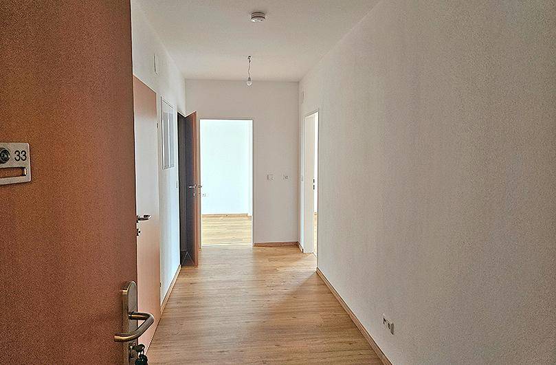Heller Flur mit Laminatboden und weiß gestrichenen Wänden, der zu weiteren Räumen führt.