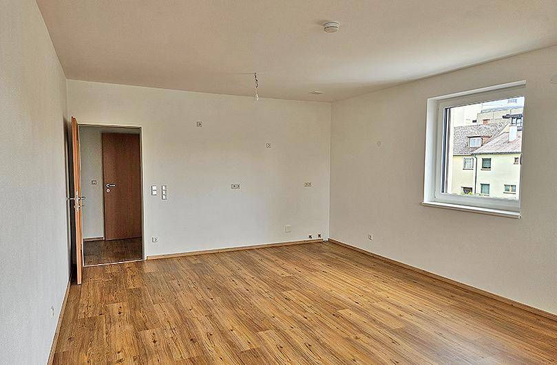 Geräumiges, leeres Zimmer mit Laminatboden und weiß gestrichenen Wänden, ideal als Wohnbereich.