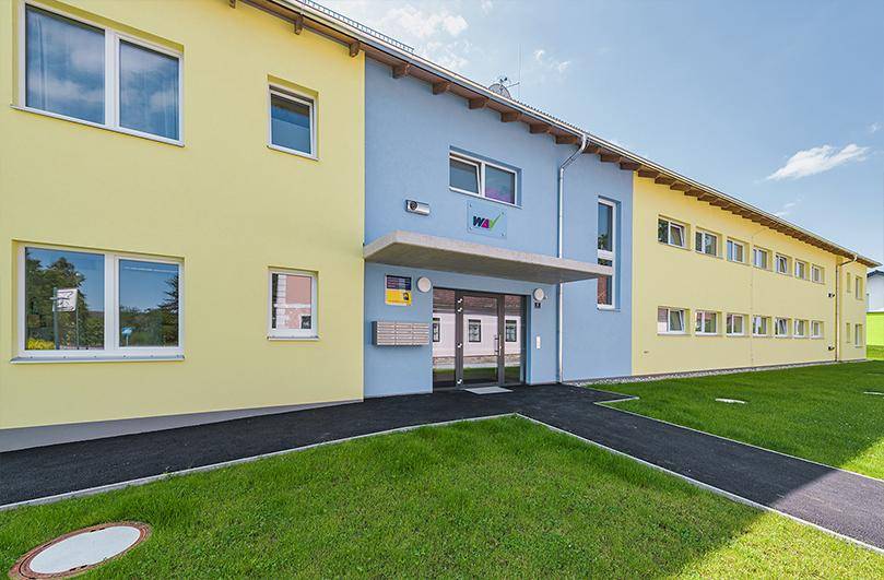 Eingangsbereich eines modernen Mehrfamilienhauses mit farbiger Fassade und Briefkästen.