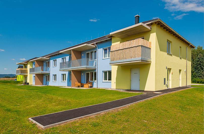 Moderne Wohnanlage mit farbigen Fassaden und Balkonen, umgeben von einer grünen Landschaft.