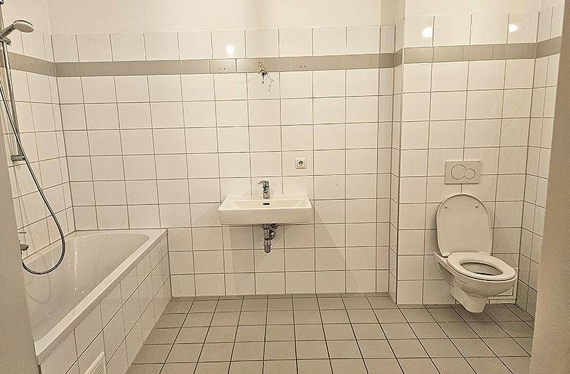Gefliestes Badezimmer mit Badewanne, Dusche, Waschbecken und wandhängendem WC.