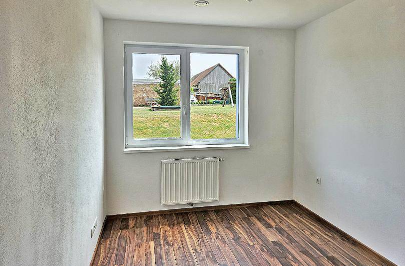 Heller Raum mit Laminatboden und einem großen Fenster mit Blick ins Grüne.