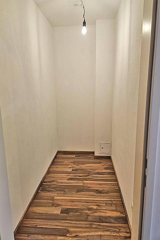 Schmaler Abstellraum mit Laminatboden und einer einfachen Deckenleuchte.